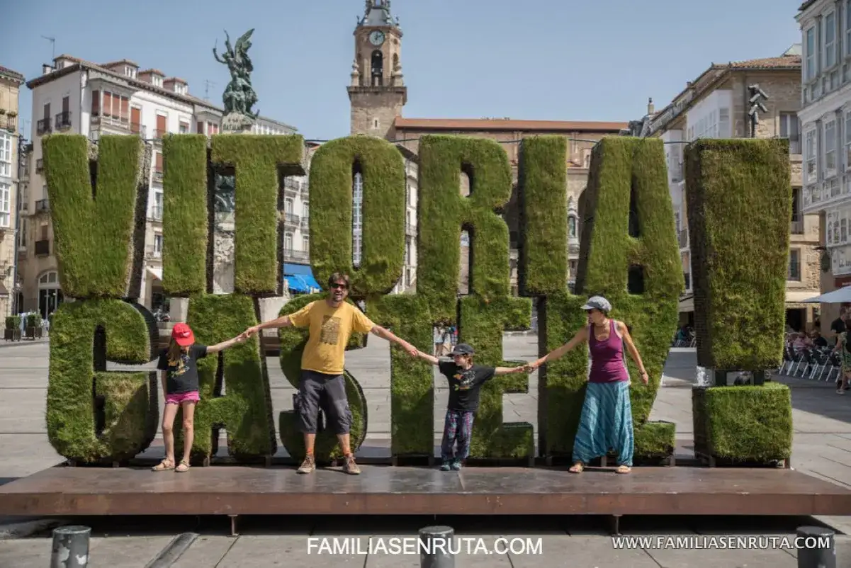 Familia disfrutando de Vitoria con ni&ntilde;os, cogidos de la mano frente a las letras gigantes de c&eacute;sped.