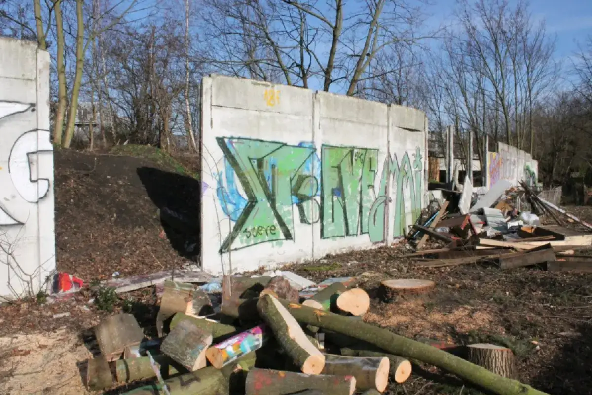 Graffiti auf den &Uuml;berresten der Berliner Mauer, umgeben von Holz und Tr&uuml;mmern.