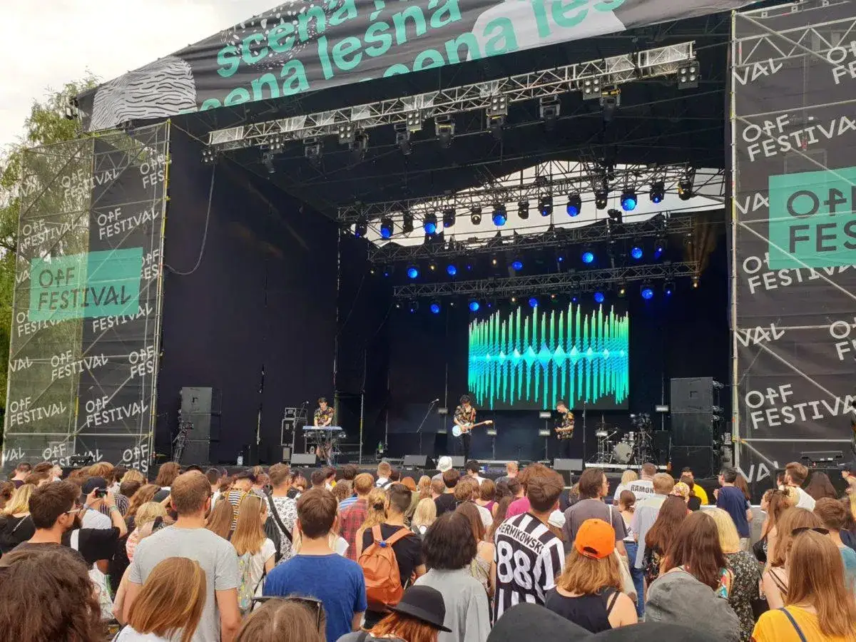 Tłum ludzi na koncercie podczas OFF Festival Katowice. Na scenie gra zesp&oacute;ł, a za nim wyświetla się kolorowy ekran.