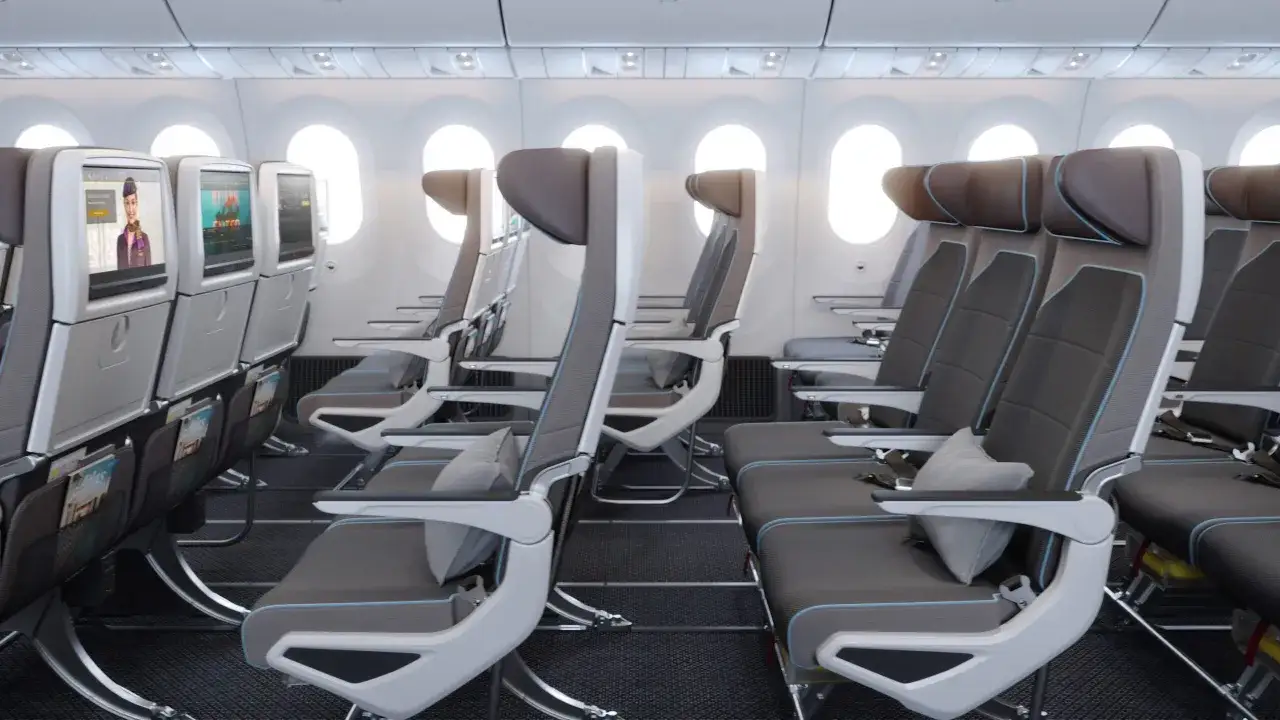 Wnętrze samolotu Etihad Airways. Fotele w rzędach, ekrany pokładowe z uśmiechniętą stewardesą. Dobre etihad airways opinie to podstawa.