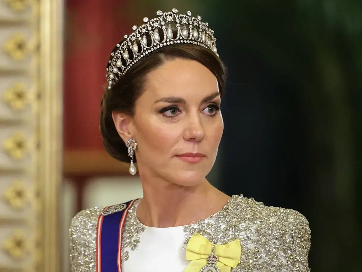 Kate Middleton, con tiara y pendientes de perlas, luce un vestido blanco bordado y una banda azul y roja.