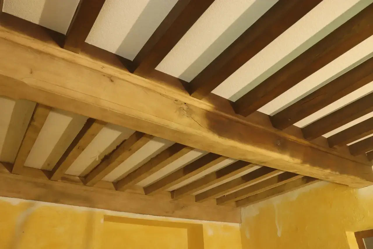Poutres en bois massif, fra&icirc;chement sabl&eacute;es, r&eacute;v&eacute;lant leur grain naturel sous un plafond blanc. Le sablage poutre bois met en valeur la beaut&eacute; rustique de la charpente.
