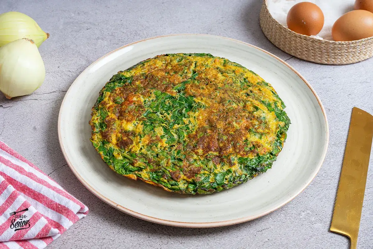 Tortilla de acelgas dorada y esponjosa, lista para disfrutar. Acompañada de cebolla y huevos frescos.