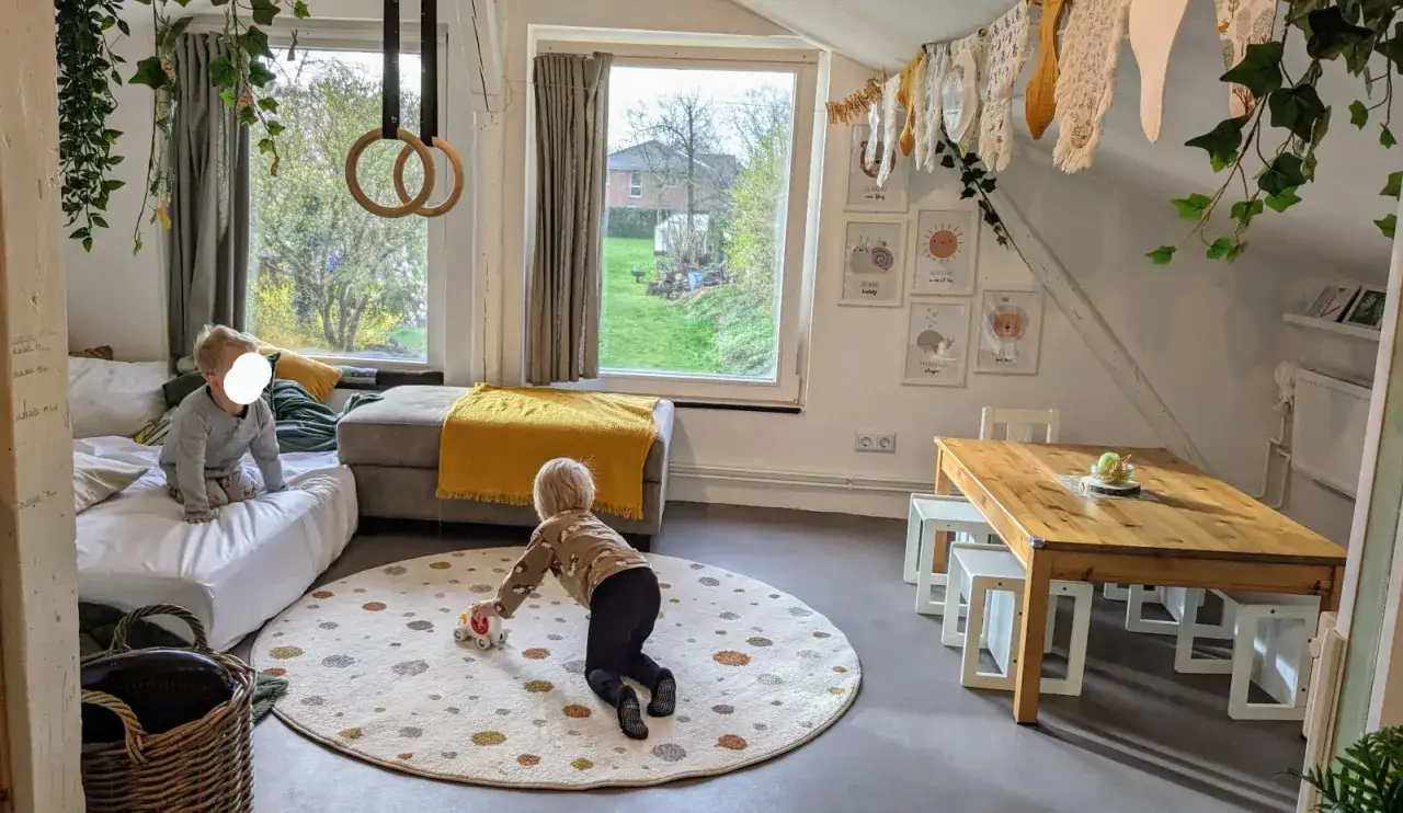 Kinder spielen in einem gemütlichen Raum, der zum **Tagesmutter werden** einlädt. Ein Kind rollt mit einem Spielzeugauto, während ein anderes auf einer Matratze sitzt.