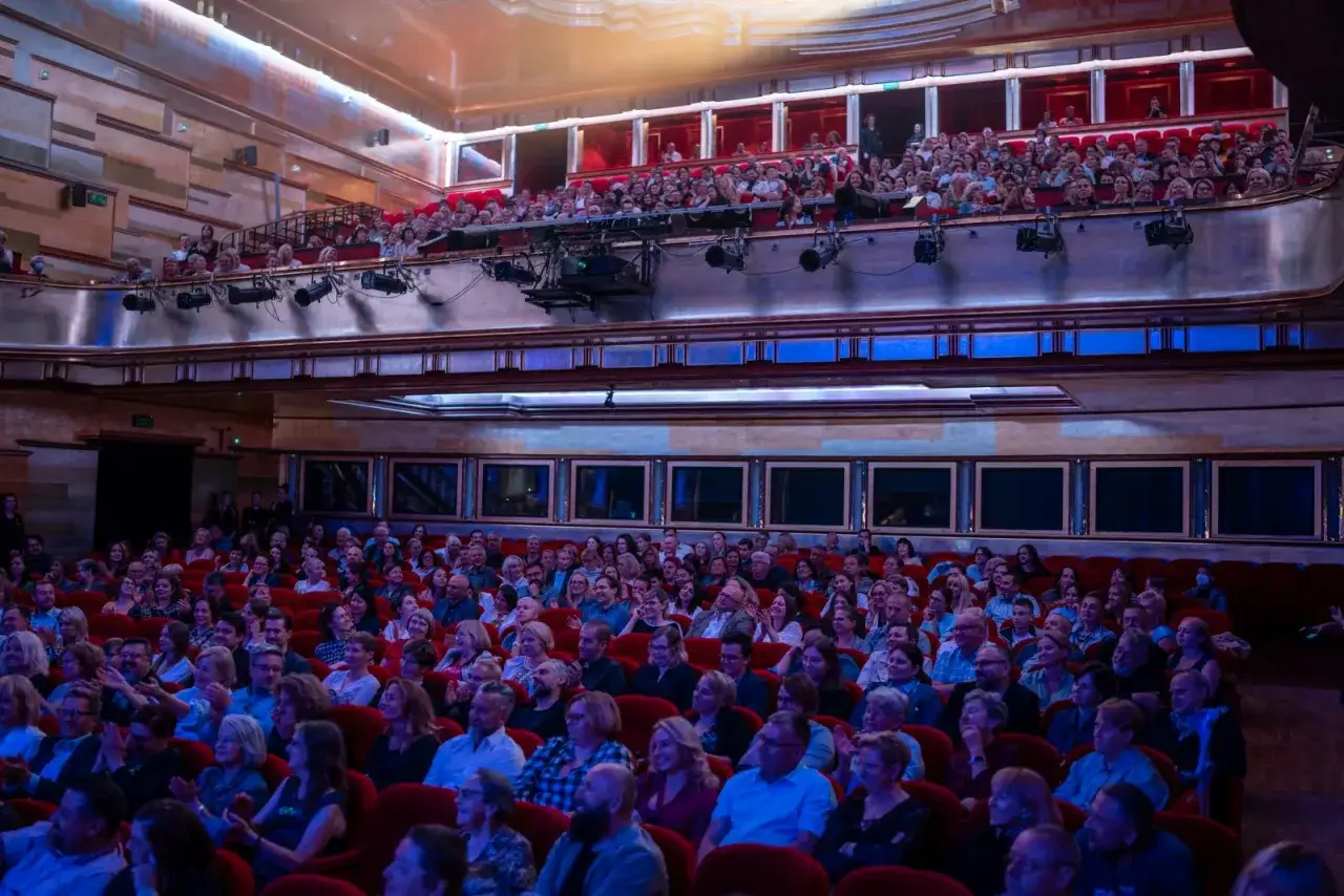 Widownia Teatru Capitol Poznań wypełniona po brzegi. Ludzie siedzą w czerwonych fotelach, czekając na spektakl.