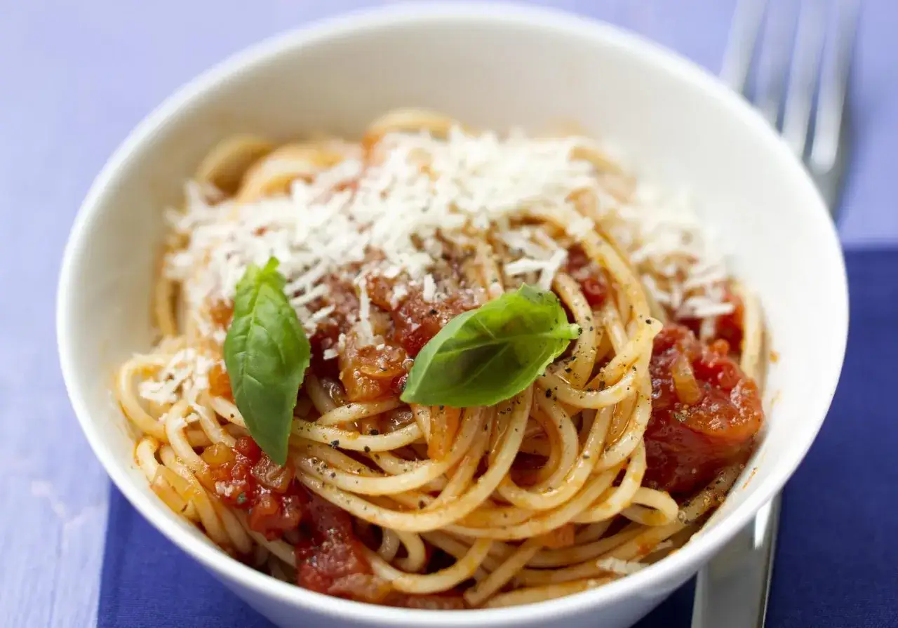 Un bol de spaghettis sauce tomate, parsemé de parmesan et de basilic frais. Les pâtes sont parfaitement al dente, prêtes à être dégustées.