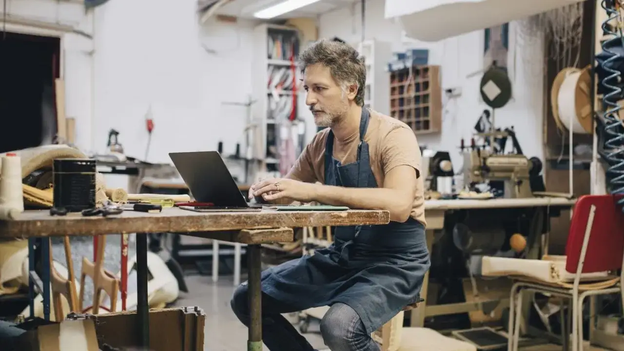 Hombre con delantal trabajando en su taller, gestionando su negocio online. Podr&iacute;a ser un **falso aut&oacute;nomo** si no tiene control real sobre su trabajo.