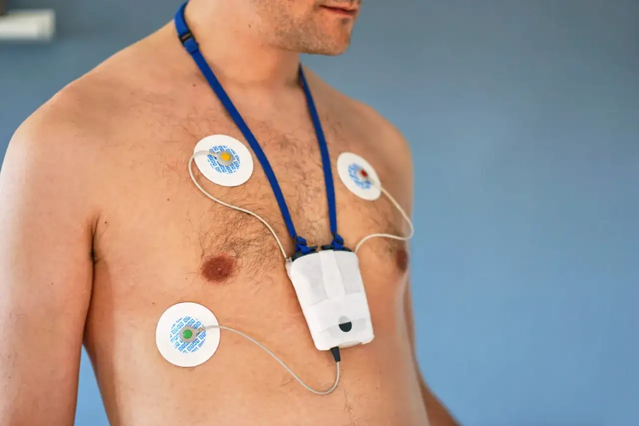 Mężczyzna z przyklejonymi elektrodami na klatce piersiowej, podłączonymi do urządzenia holter ekg na szyi.