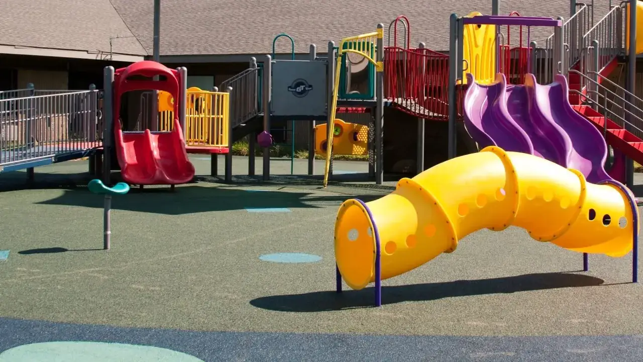 Bunter Spielplatz mit Rutschen, Tunnel und Klettergerüsten. Ein gelber Tunnel schlängelt sich über den weichen Boden, bereit für Abenteuer.