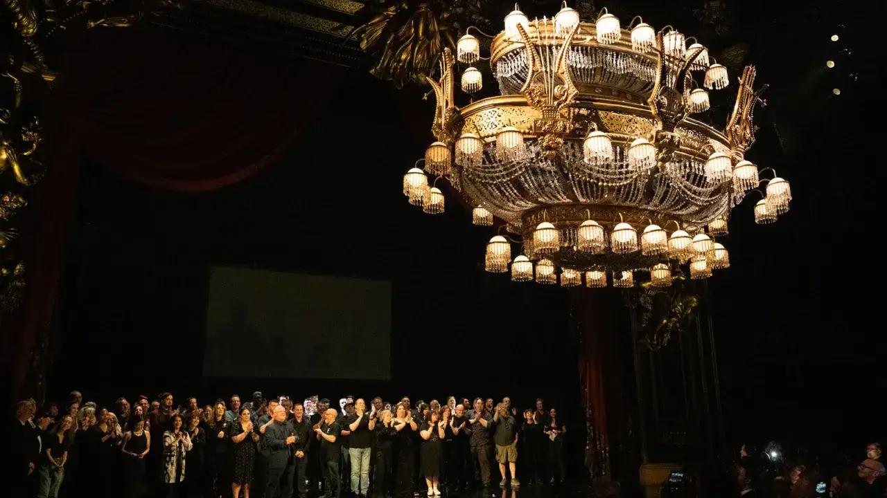 Upiór w operze: scena z wielkim żyrandolem i zespołem na deskach teatru.