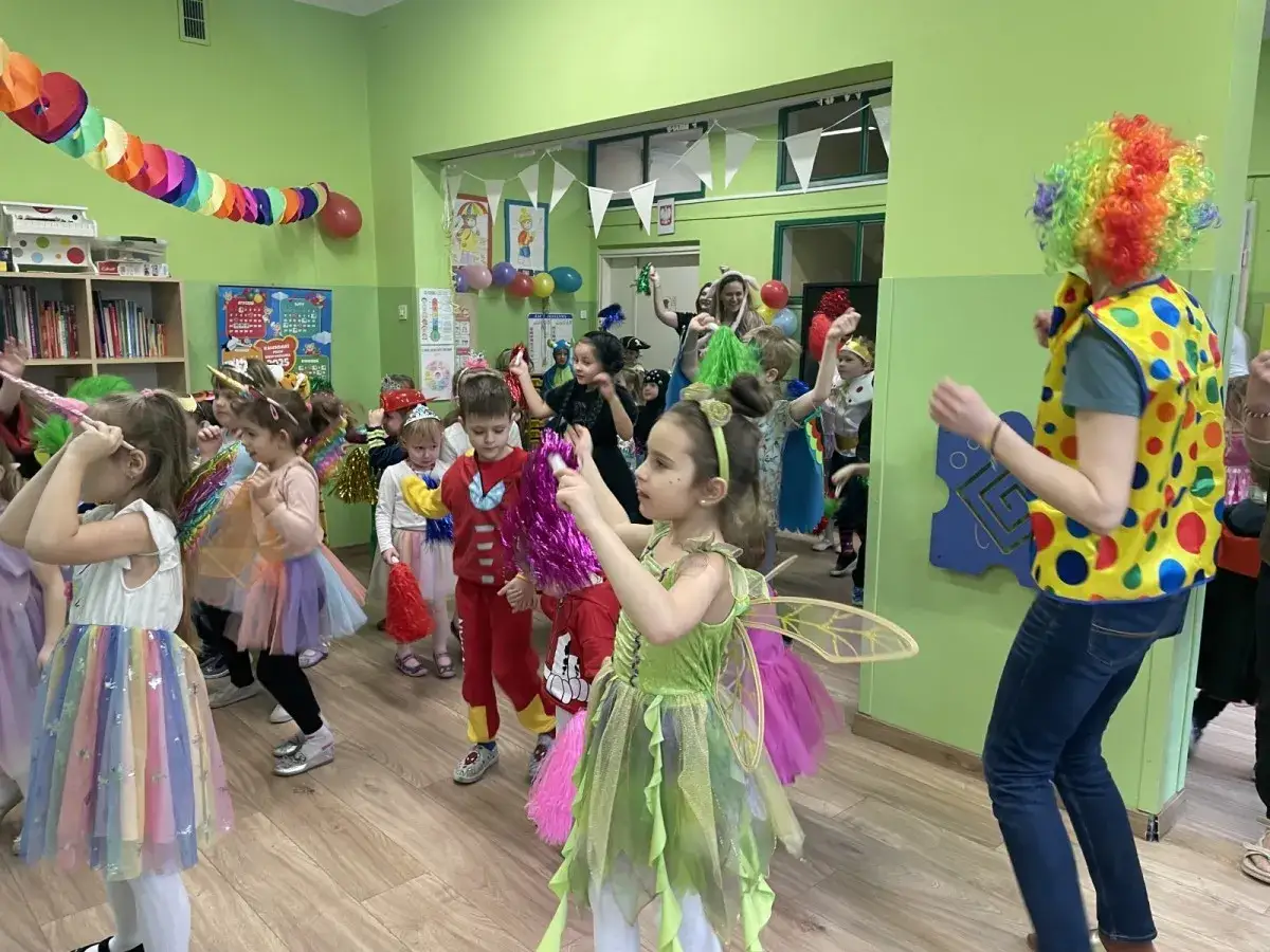 Dzieci w barwnych strojach wróżek i superbohaterów bawią się na balu karnawałowym. Wesołe zabawy na balu karnawałowym dla dzieci trwają w najlepsze!