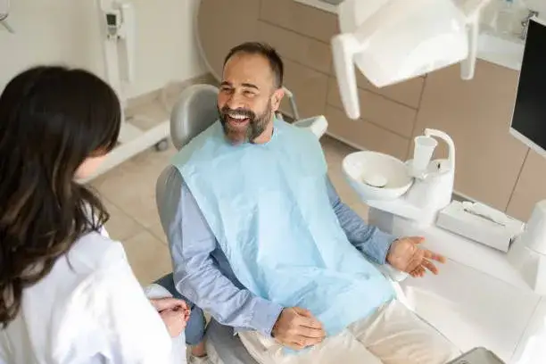 Pacjent rozmawiający z dentystą w gabinecie, uśmiechnięty dentysta