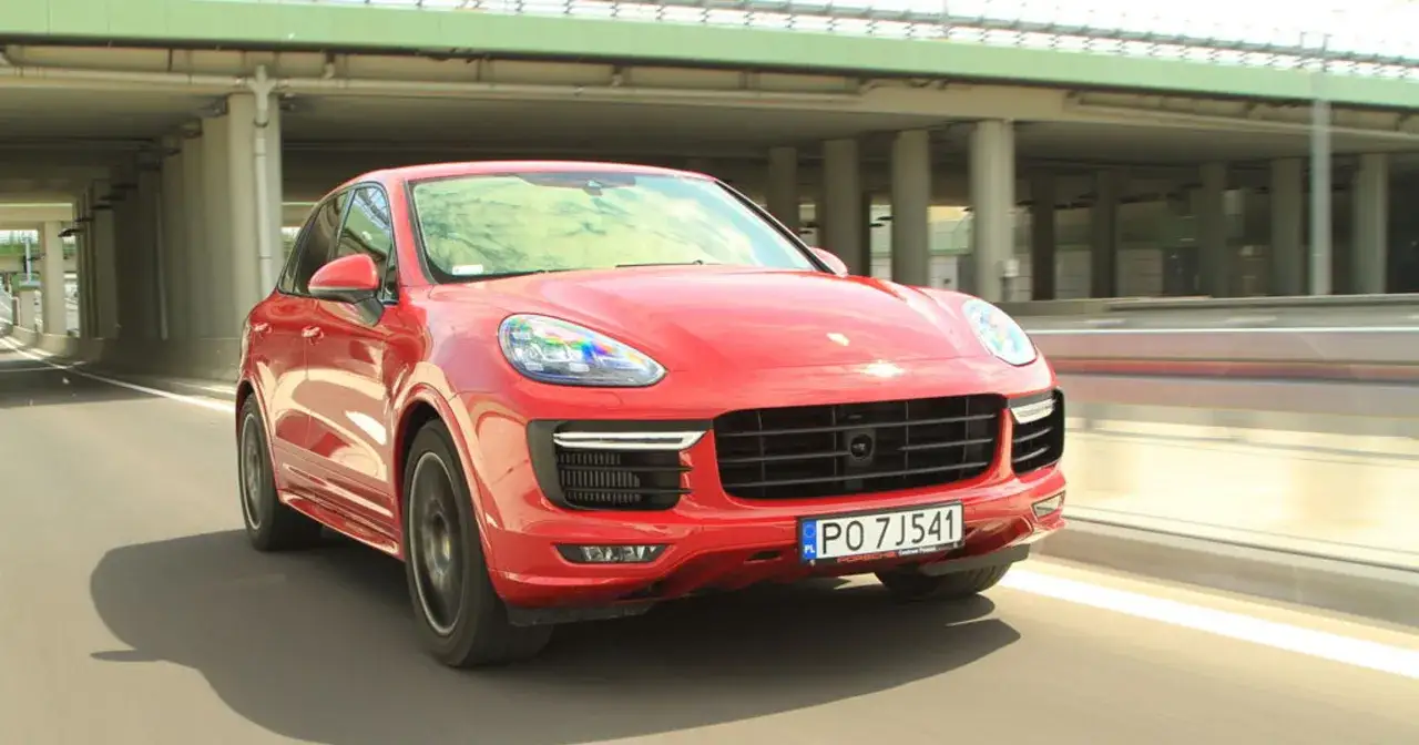Czerwony Porsche Cayenne GTS pędzi po drodze pod estakadą.