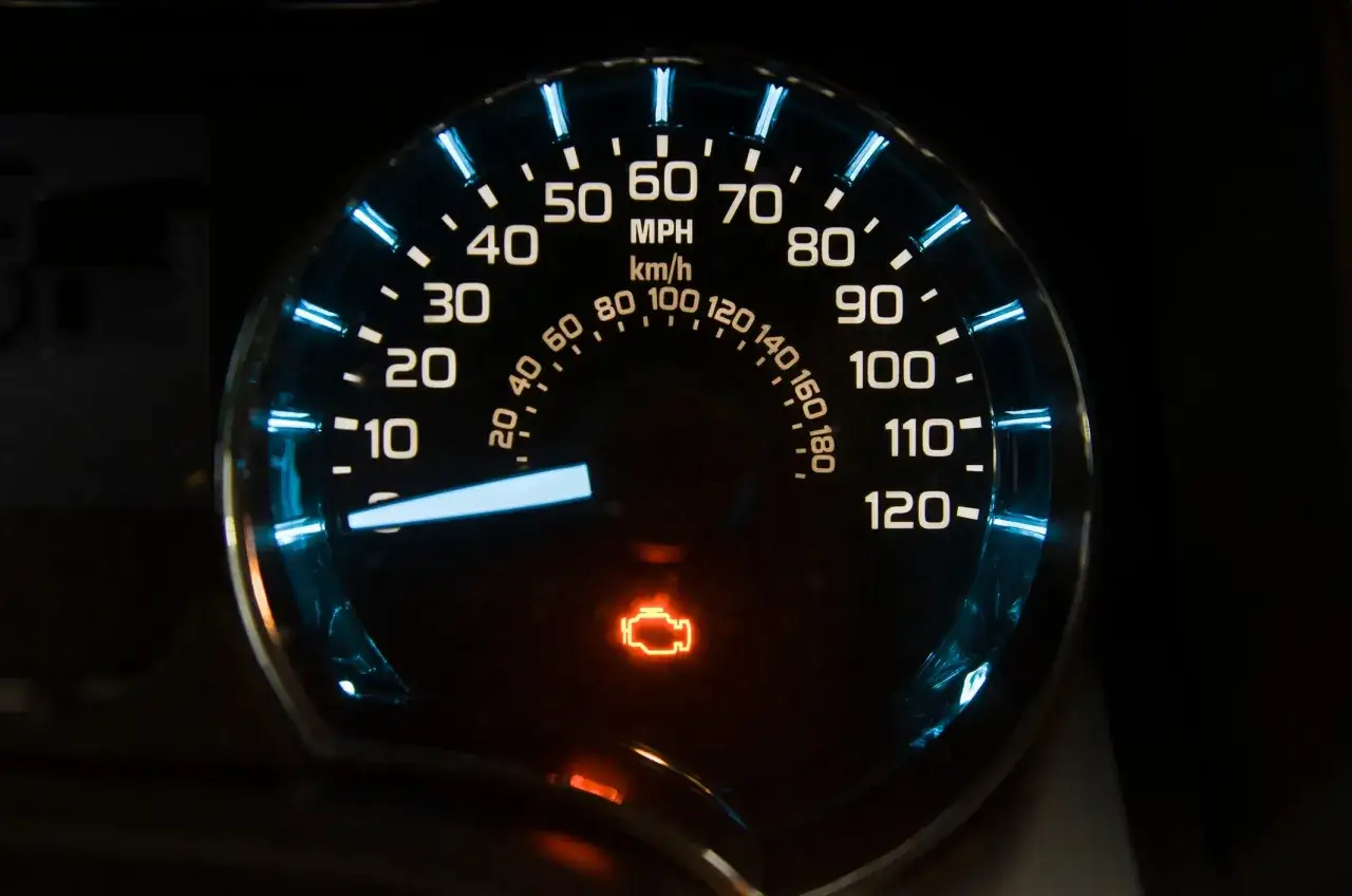 Car dashboard with illuminated speedometer and an orange engine warning light. This image hints at how to read engine codes without a reader.