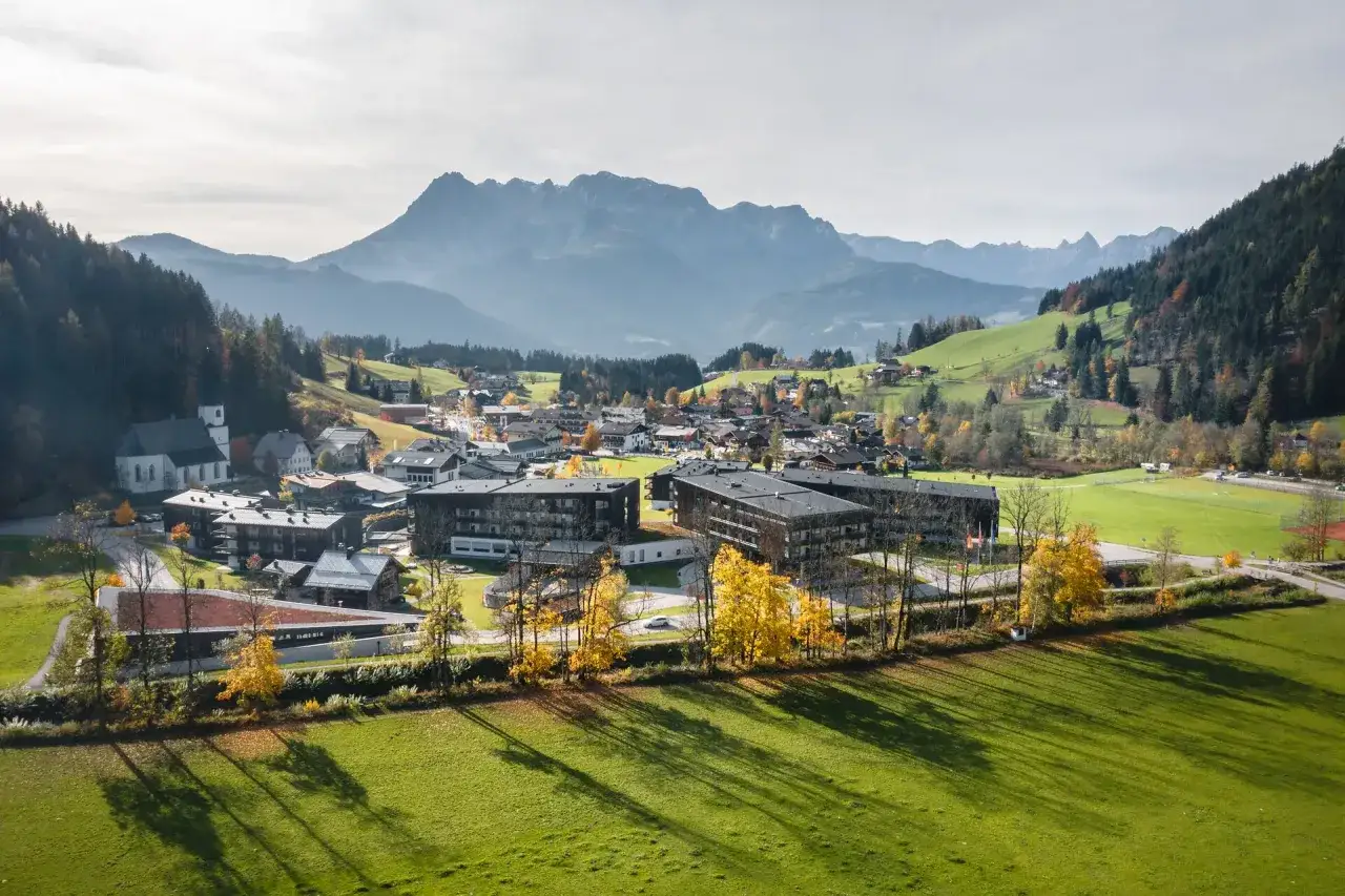Herbstliche Idylle in Aja Wörthwerfen: Moderne Gebäude und traditionelle Häuser vor imposanter Bergkulisse.