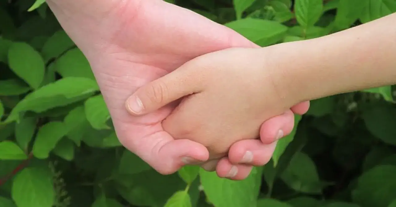 Un adulto e un bambino si tengono per mano. Il loro sfiorarsi le mani significato &egrave; un gesto di amore e protezione.