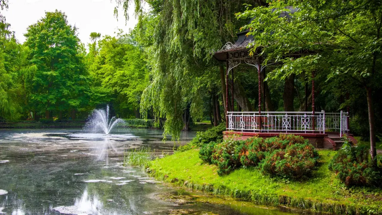 Piła miasto: malowniczy park z fontanną i altanką nad stawem, otoczony bujną zielenią.