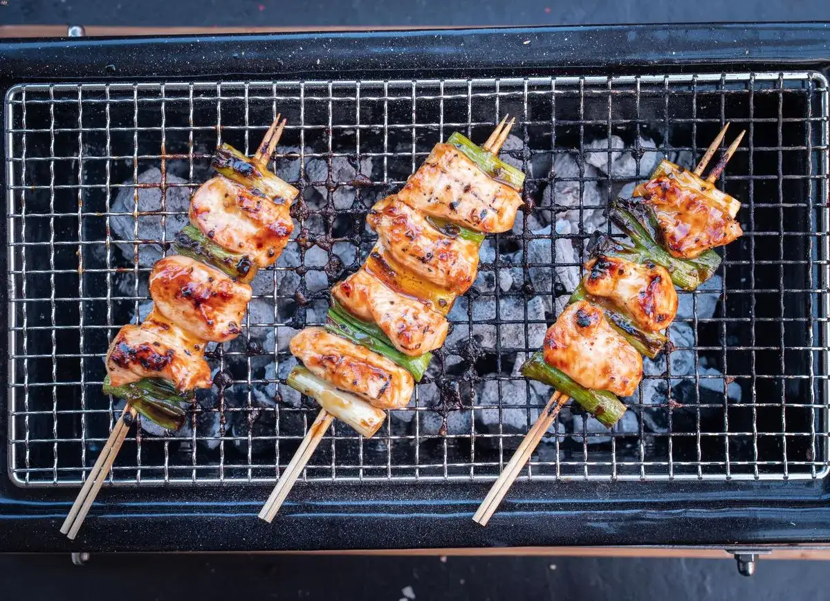 Drei saftige Yakitori-Spie&szlig;e mit H&auml;hnchen und Lauch brutzeln auf einem Holzkohlegrill.
