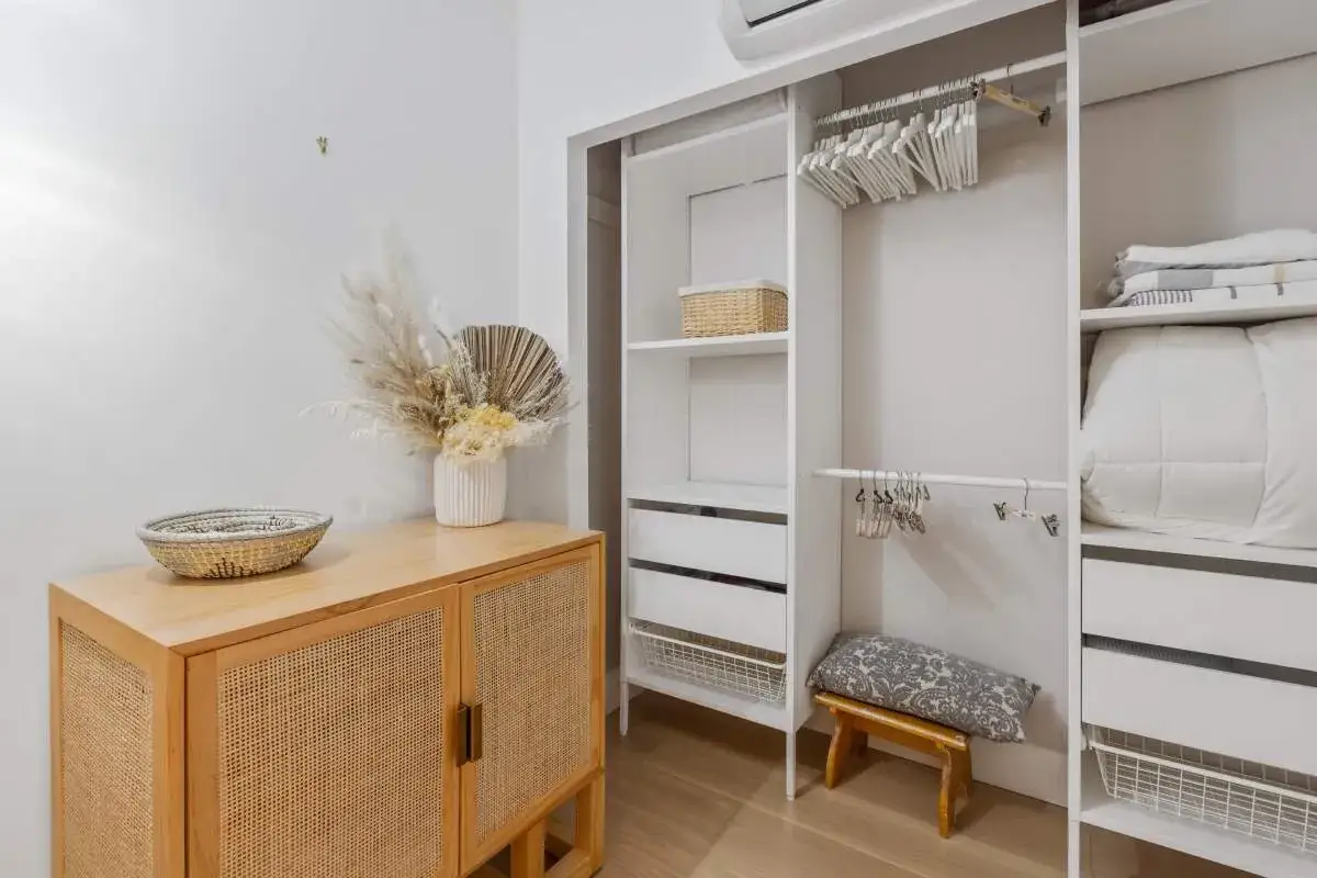 Armario blanco con ropa doblada y perchas. Un mueble de madera con cesta y jarr&oacute;n con flores secas. Ideas para como quitar el olor a humedad de un armario.