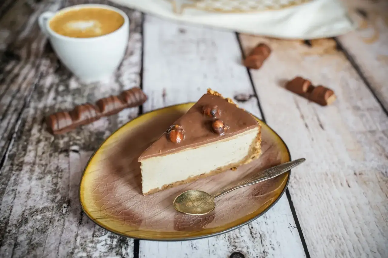 Pyszny sernik Kinder Bueno z orzechami na wierzchu, obok filiżanka kawy i batoniki.