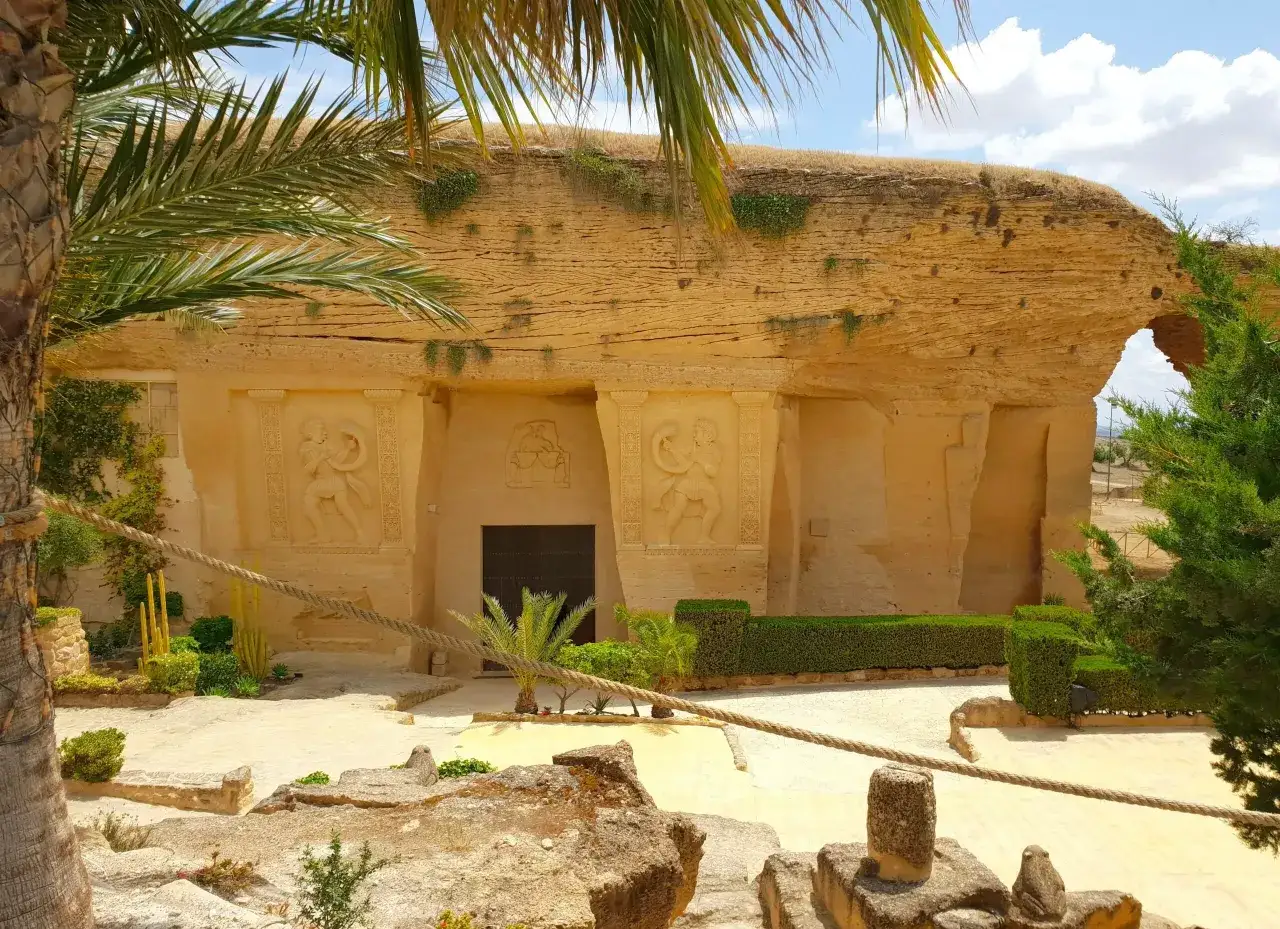 Descubre la historia en Osuna: una entrada tallada en roca con relieves, palmeras y un patio soleado. &iexcl;Imprescindible que ver en Osuna!