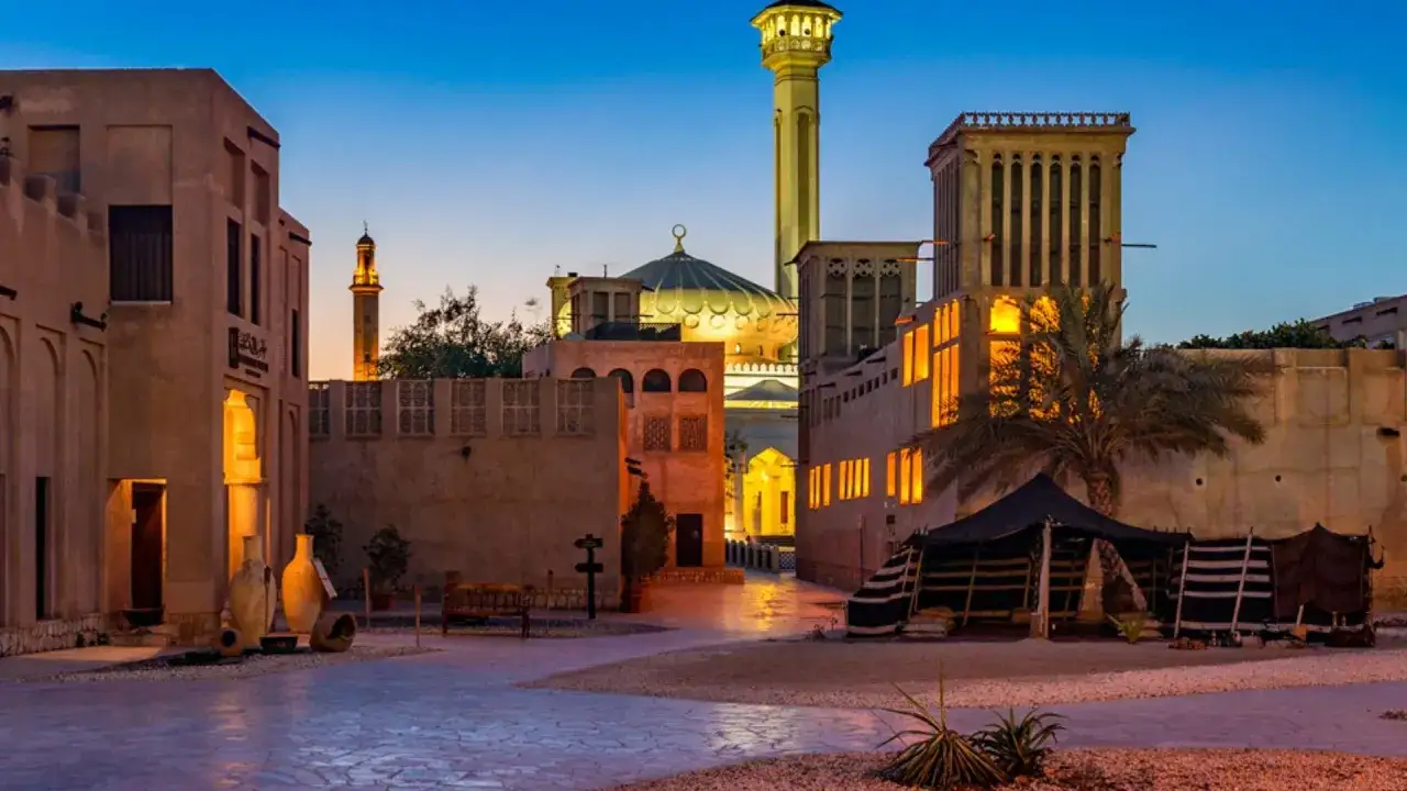 Ein Blick auf Dubai vor 100 Jahren: traditionelle Lehmhäuser, eine Moschee und Zelte im Abendlicht.