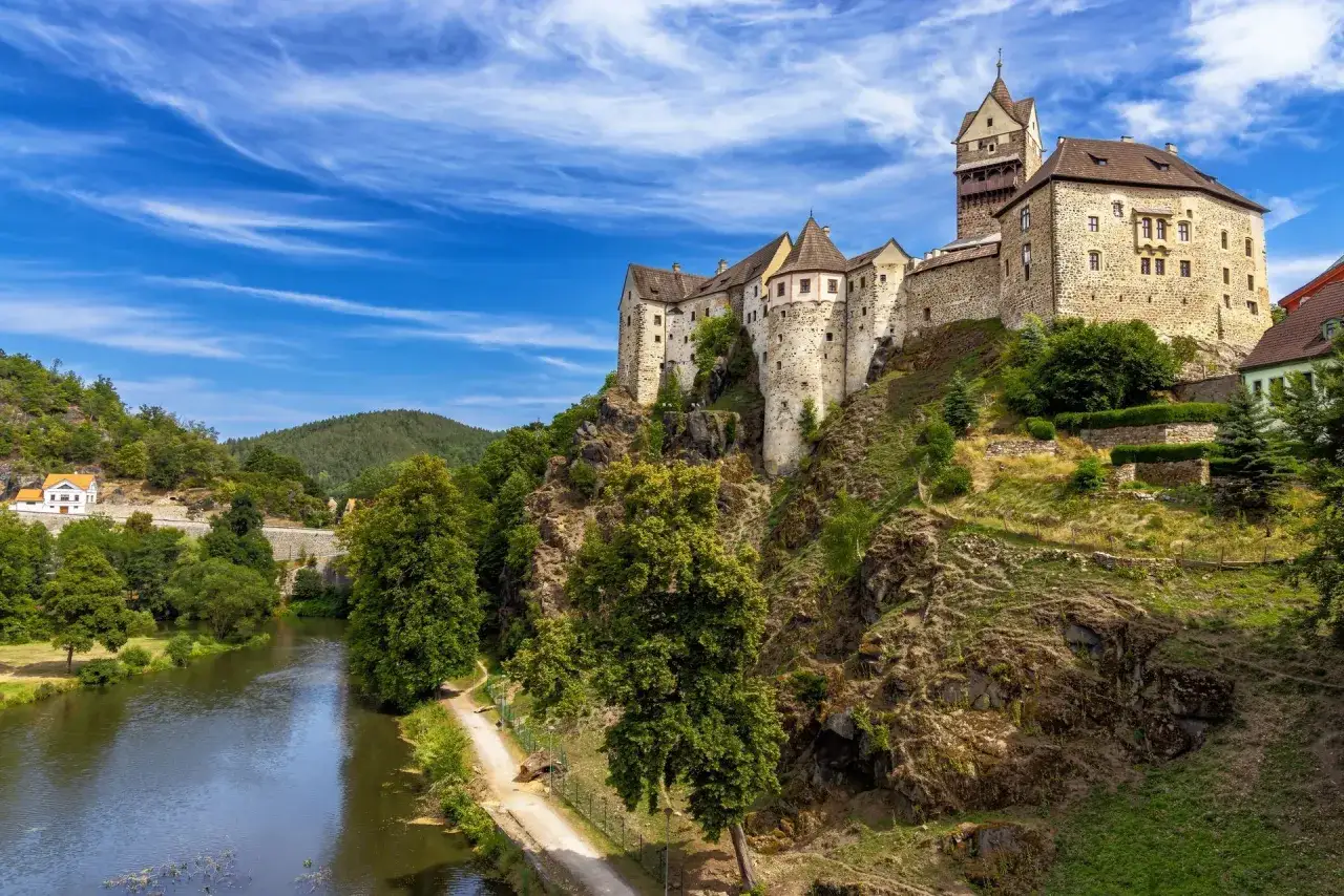Zamek na skale w Czechach, symbol bohemii, góruje nad rzeką i zielonymi wzgórzami.