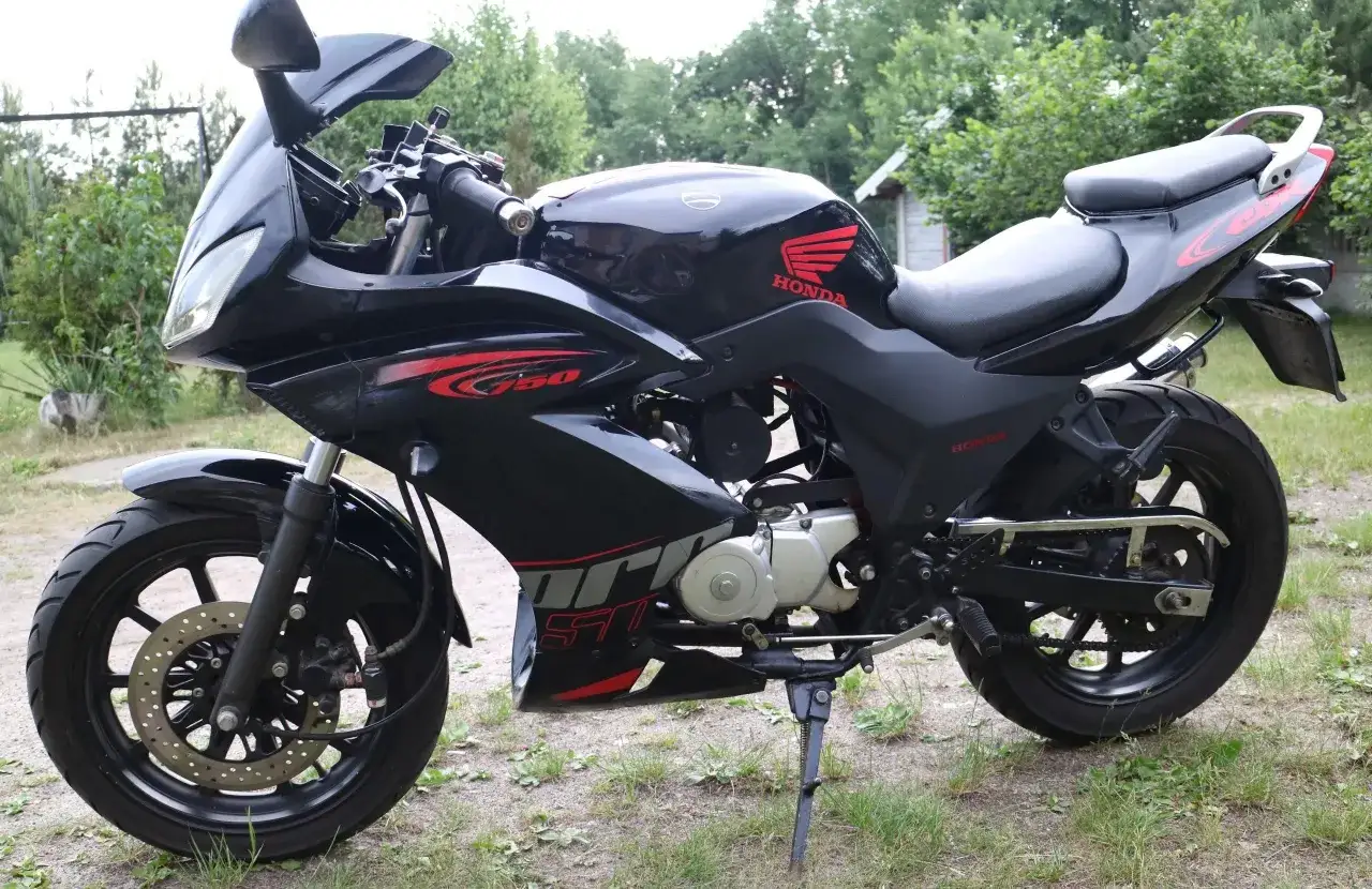 Czarny motocykl Zipp Xrace 50 z czerwonymi akcentami, zaparkowany na trawie.