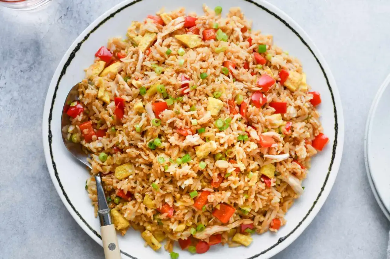 En stor portion arroz chaufa med kyckling, &auml;gg och r&ouml;d paprika, toppad med salladsl&ouml;k.