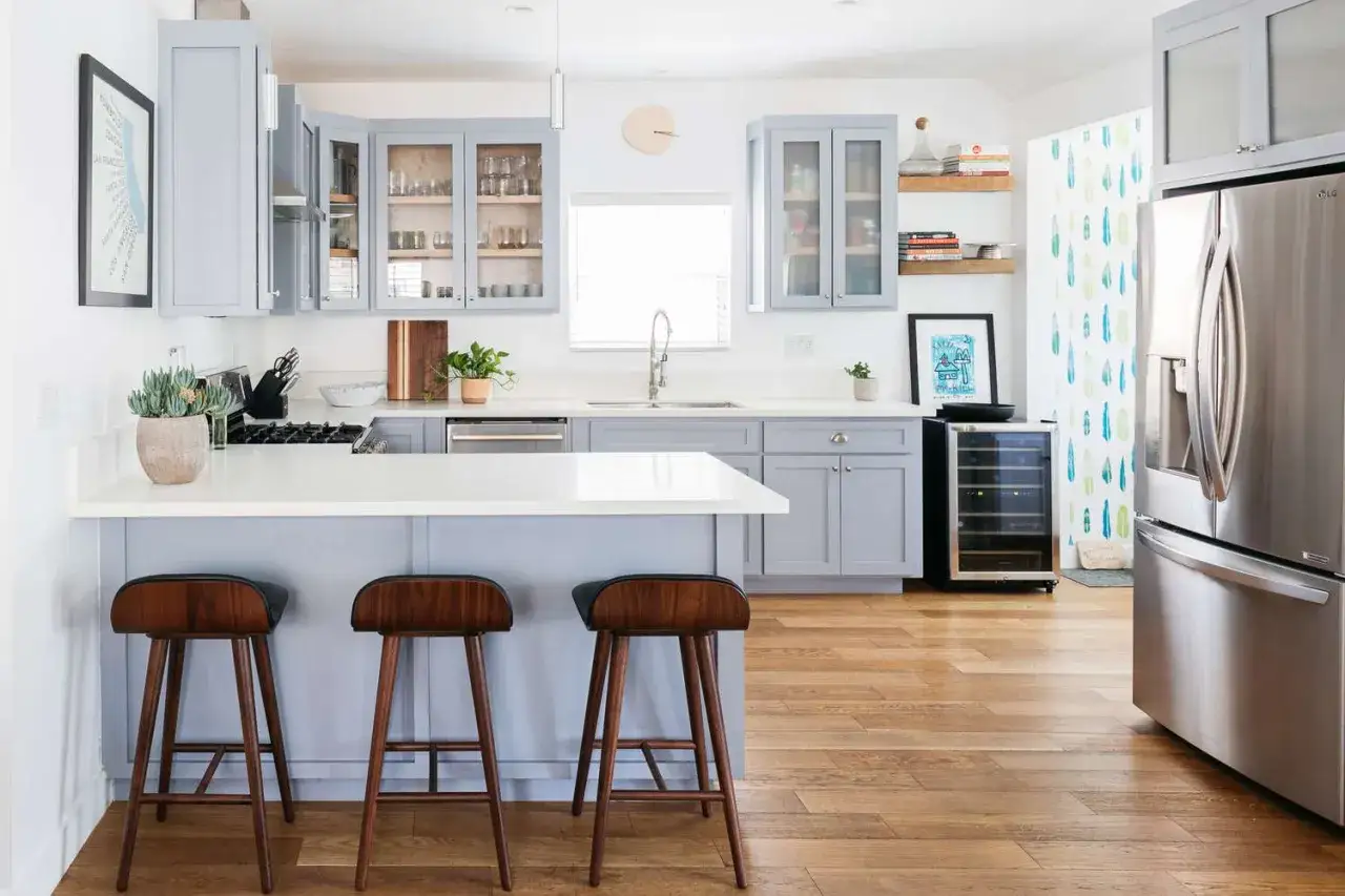 Cuisine 8m2 moderne avec &icirc;lot central, tabourets en bois, armoires grises et r&eacute;frig&eacute;rateur en inox.
