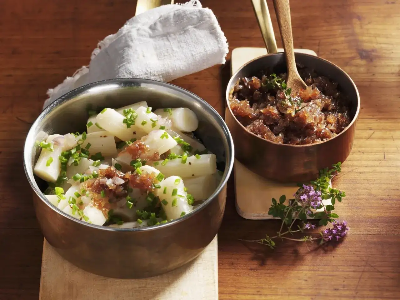 Haferwurzel-Rezept: Gekochte Haferwurzelstücke mit Schnittlauch und karamellisierten Zwiebeln in Kupferkesseln, garniert mit Thymian.