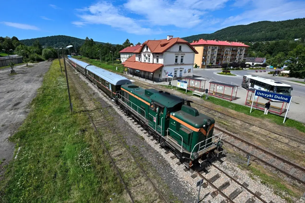 Zielona lokomotywa z wagonami na stacji Ustrzyki Dolne, gotowa na podróż pociągiem w Bieszczady.