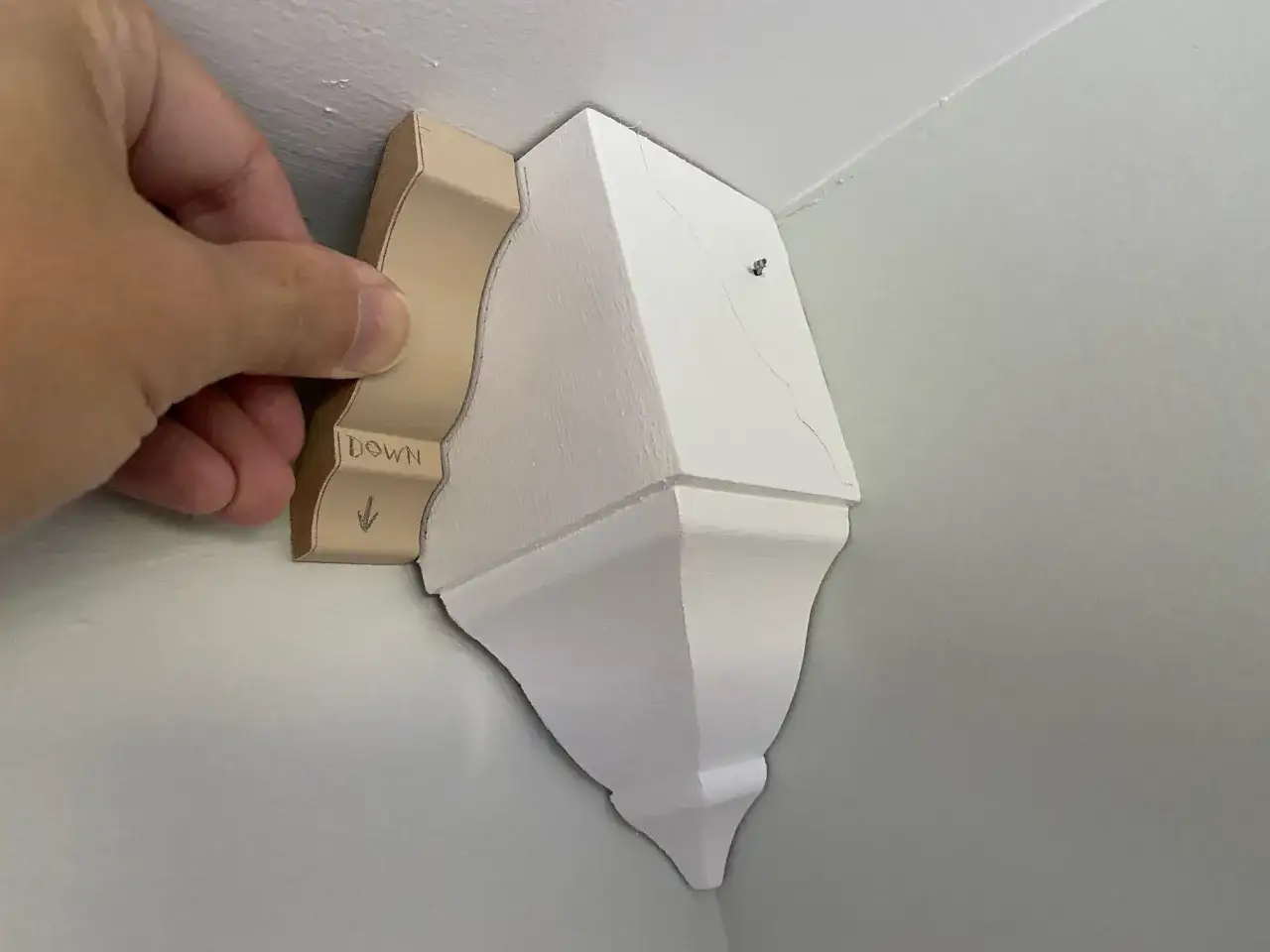 A hand holds a jig for crown molding installation, showing the 