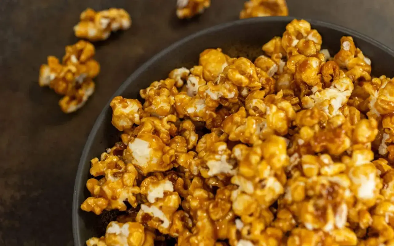 Un bol rempli de pop corn sucr&eacute;, enrob&eacute; d'une sauce caramel dor&eacute;e et brillante. Quelques grains s'&eacute;chappent sur le fond sombre.