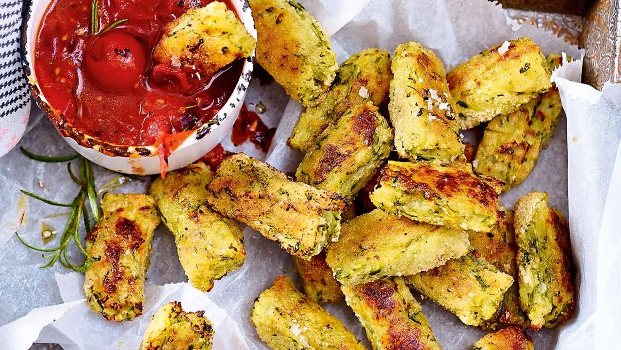Knusprige zucchini frikadellen, goldbraun gebacken, liegen neben einer Schale mit Tomatensauce. Ein leckerer Snack!