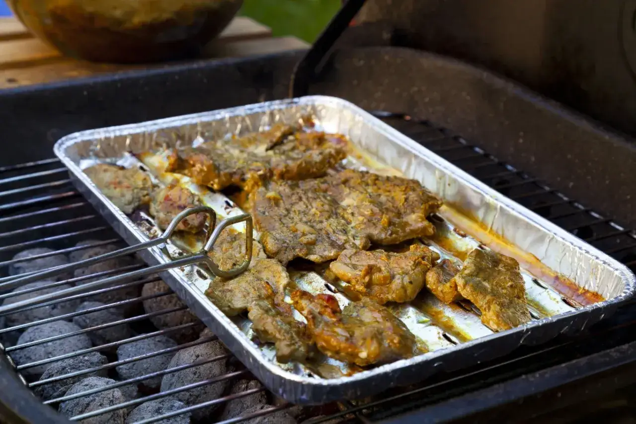 Karkówka w domowej marynacie piecze się na grillu w aluminiowej tacce.