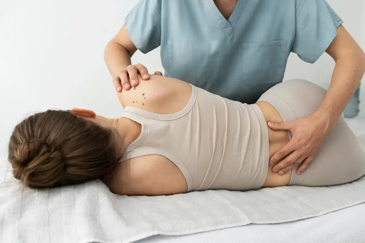 Fizjoterapeuta bada plecy pacjentki, która leży na boku. Może to być związane z pytaniem: dyskopatia co to jest i jak sobie z nią radzić.