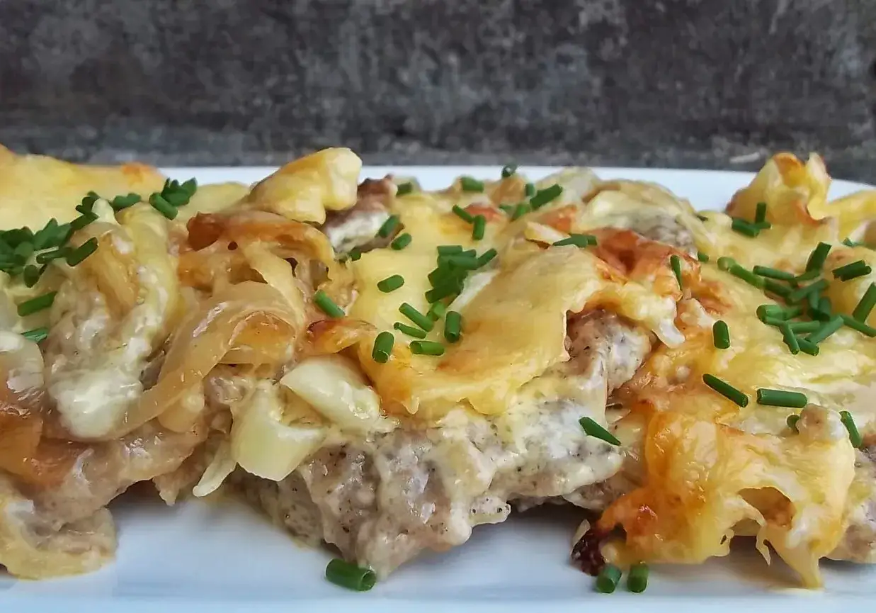 Pyszny kotlet po kowalsku, zapieczony z serem i cebulką, posypany szczypiorkiem.