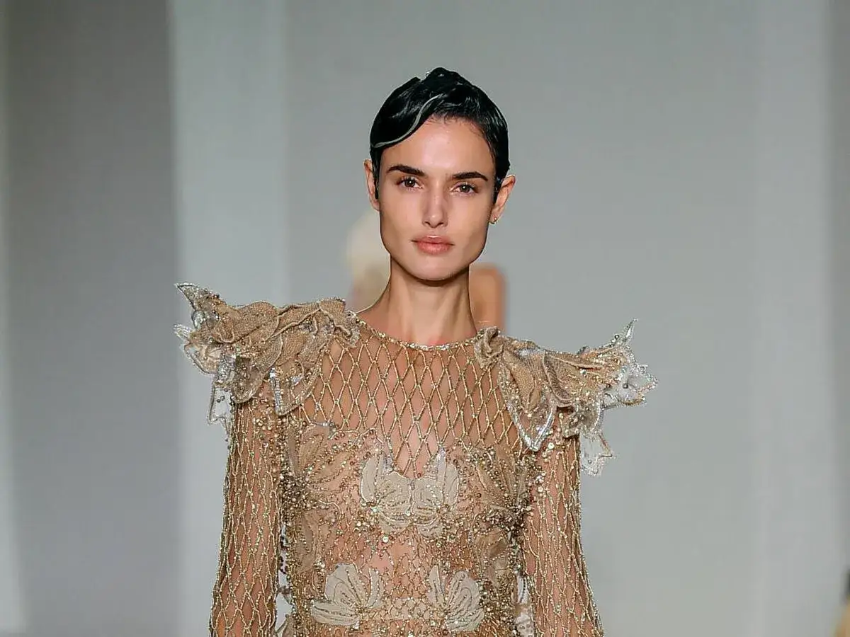 Belen Corsini desfila con un vestido dorado de pedrer&iacute;a y volantes en los hombros, un dise&ntilde;o que evoca la elegancia de la alta costura.