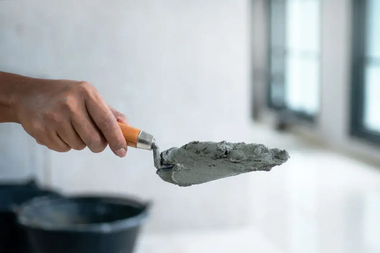 Dłoń trzyma kielnię z zaprawą, przygotowując się do pracy. Dowiedz się, jak zrobić suchy beton.