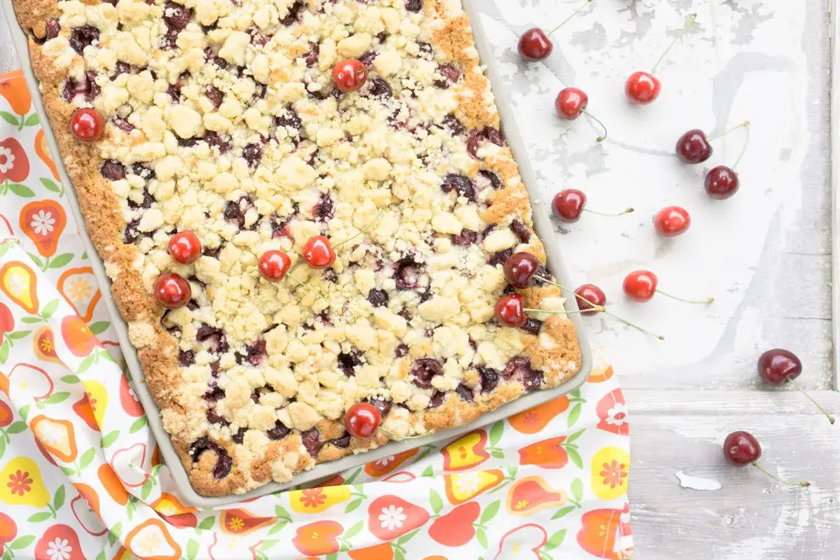 Ein saftiger Kirschstreuselkuchen im Blech, garniert mit frischen Kirschen.