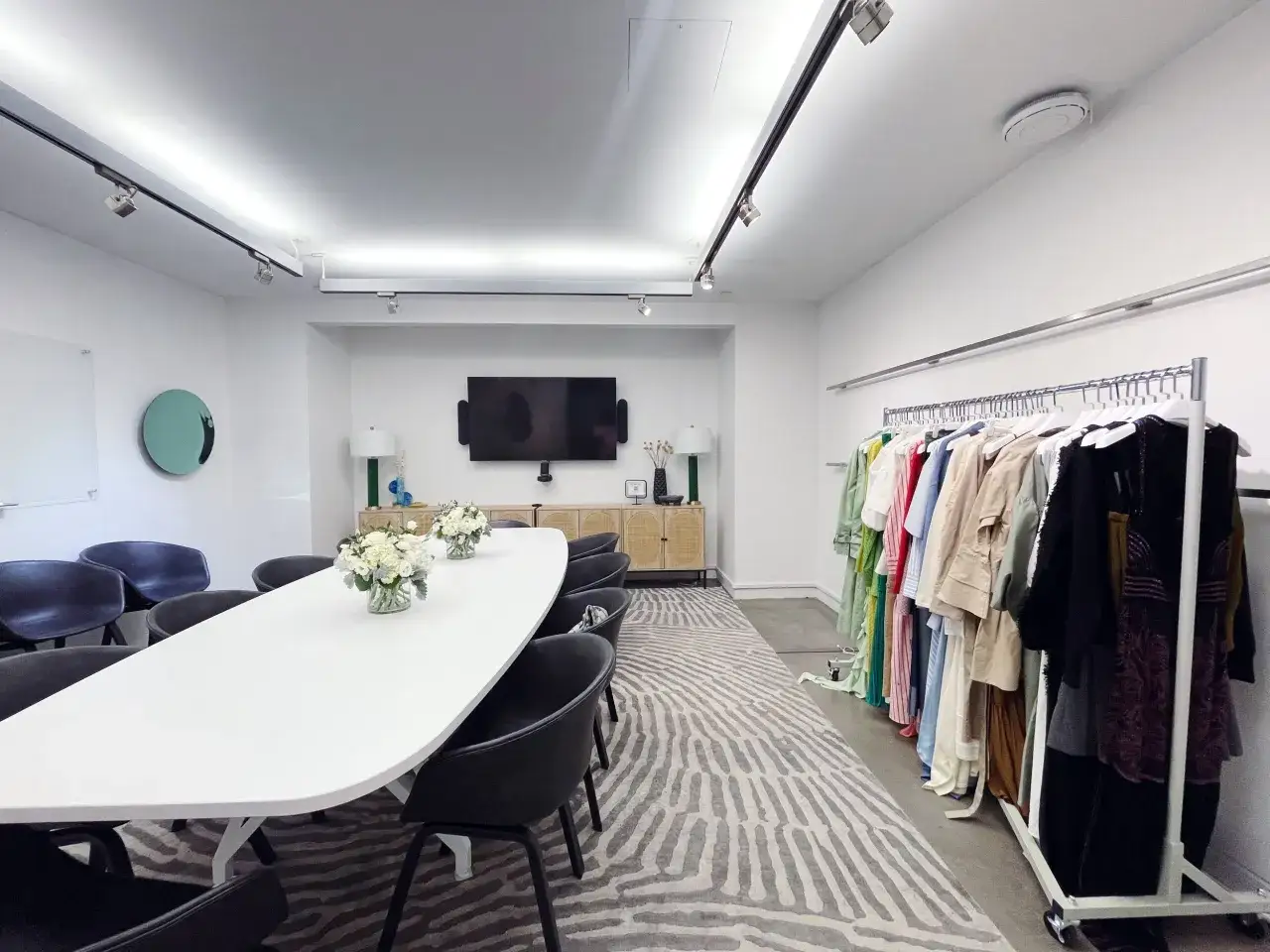 Un showroom de ropa moderno con un gran mesa de conferencias, sillas negras y percheros llenos de prendas coloridas.