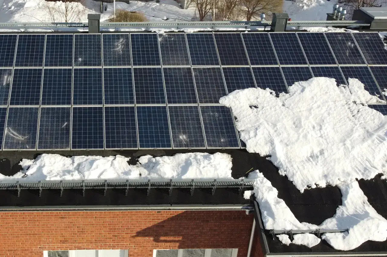 Solceller p&aring; ett tak, delvis t&auml;ckta av sn&ouml;. Trots vintern visar installationen p&aring; solcellers h&aring;llbarhet och potential f&ouml;r framtida energiproduktion.