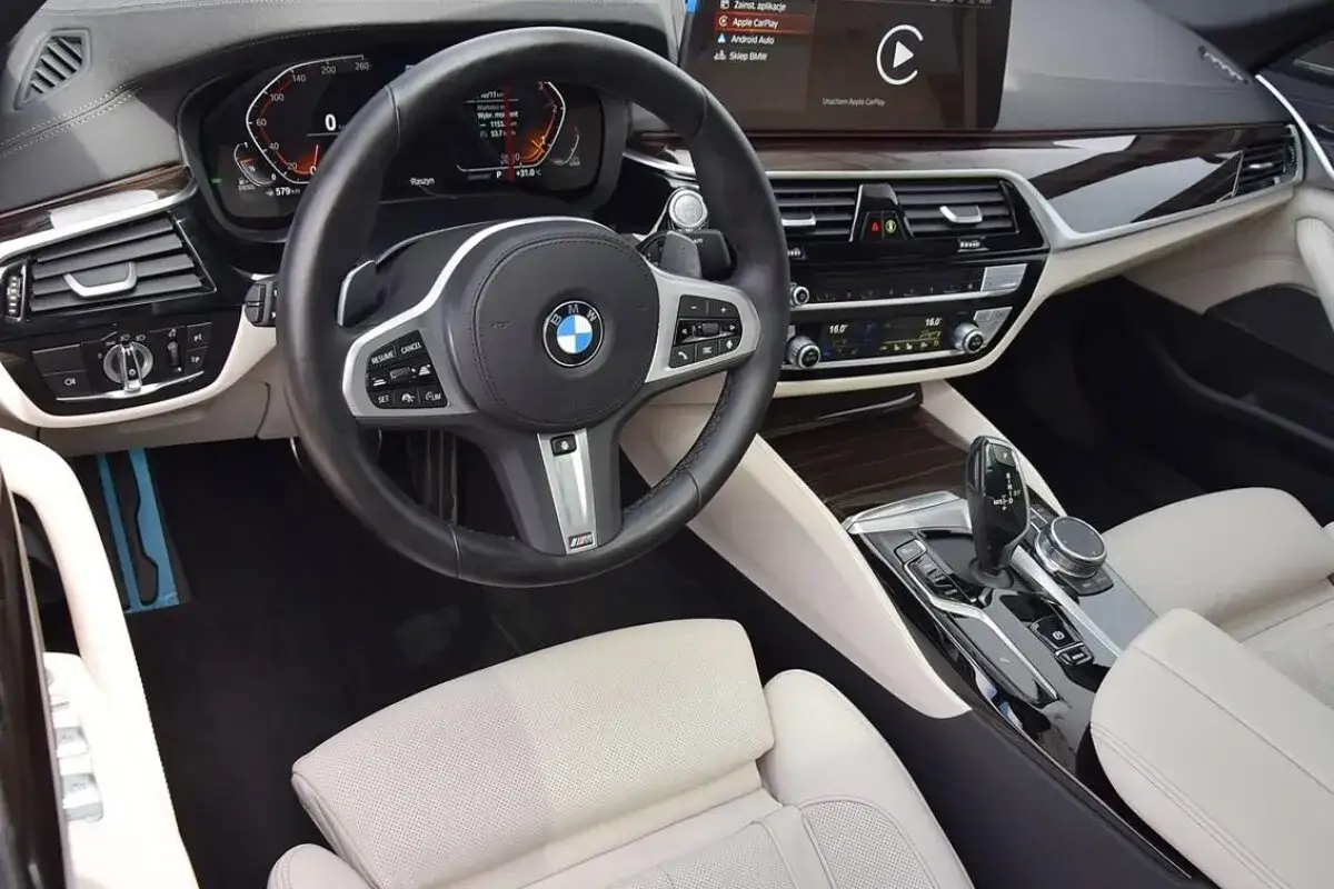 Wnętrze BMW 5 G30 z jasną tapicerką, multimediami i cyfrowymi zegarami.
