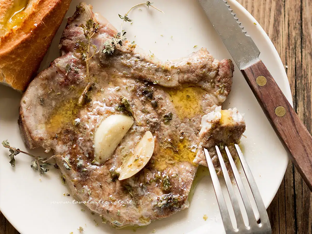 Succulenta braciola di maiale cotta con aglio e erbe aromatiche, servita con pane croccante.