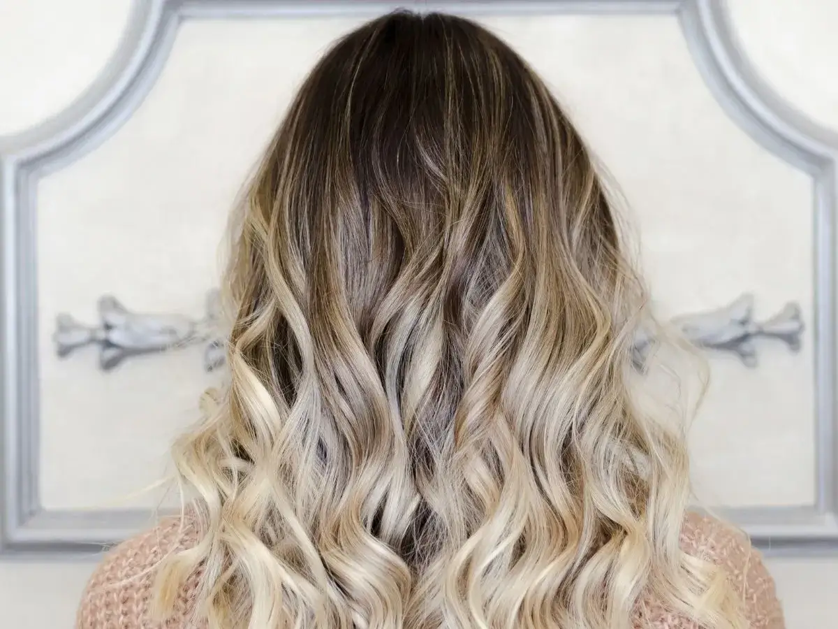 Piękne, falowane włosy z efektem ombre blond, przechodzące od ciemnych u nasady do jasnych końcówek.