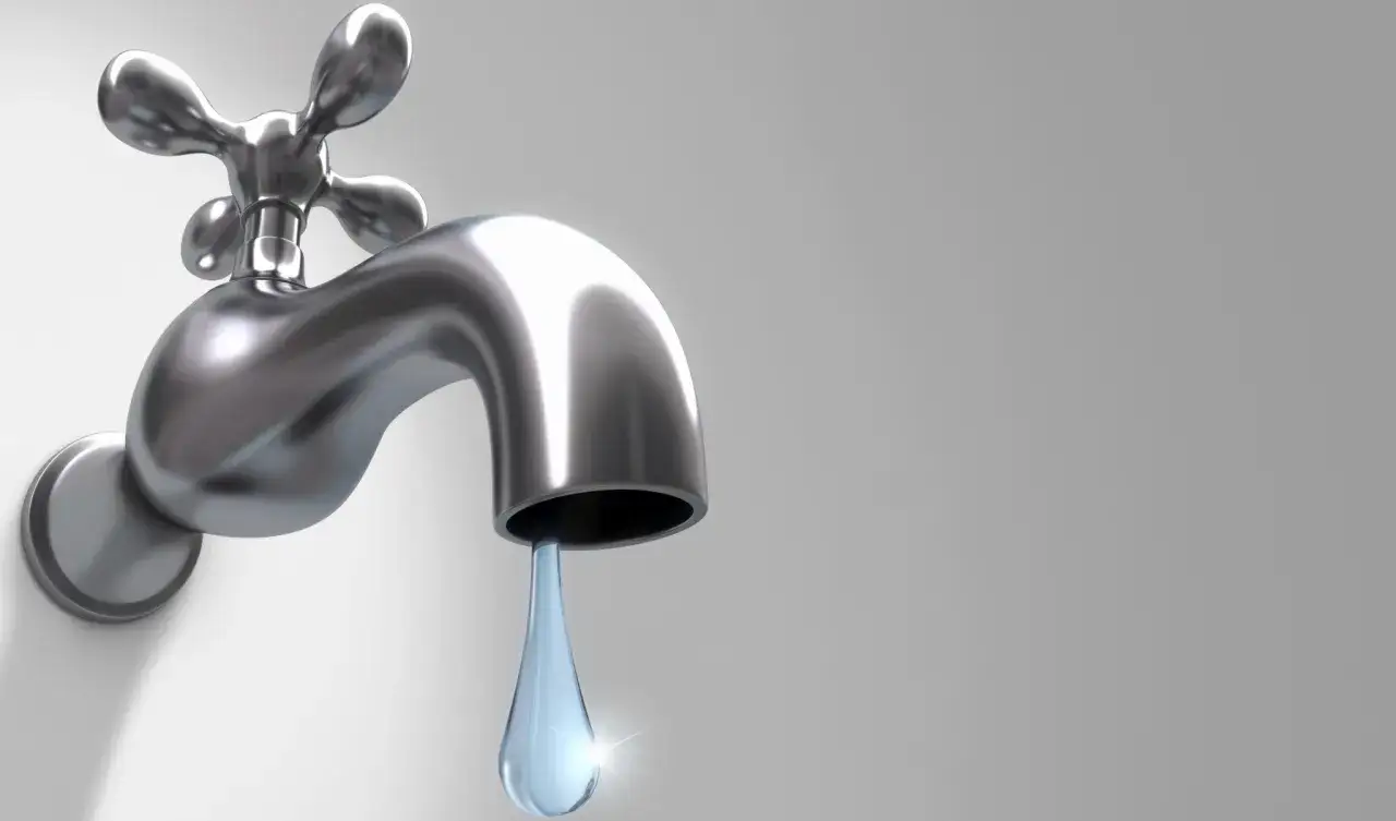 Rubinetto che perde, una goccia d'acqua trasparente cade lentamente, simbolo di spreco.