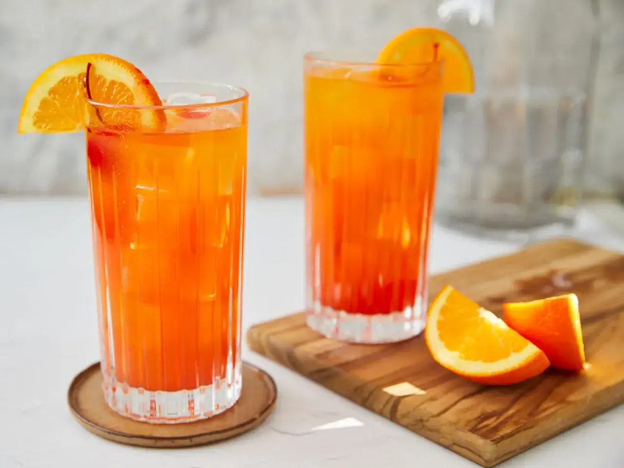 Två glas med en färggrann tequila sunrise, garnerade med apelsinskivor. Perfekt för en solig dag.