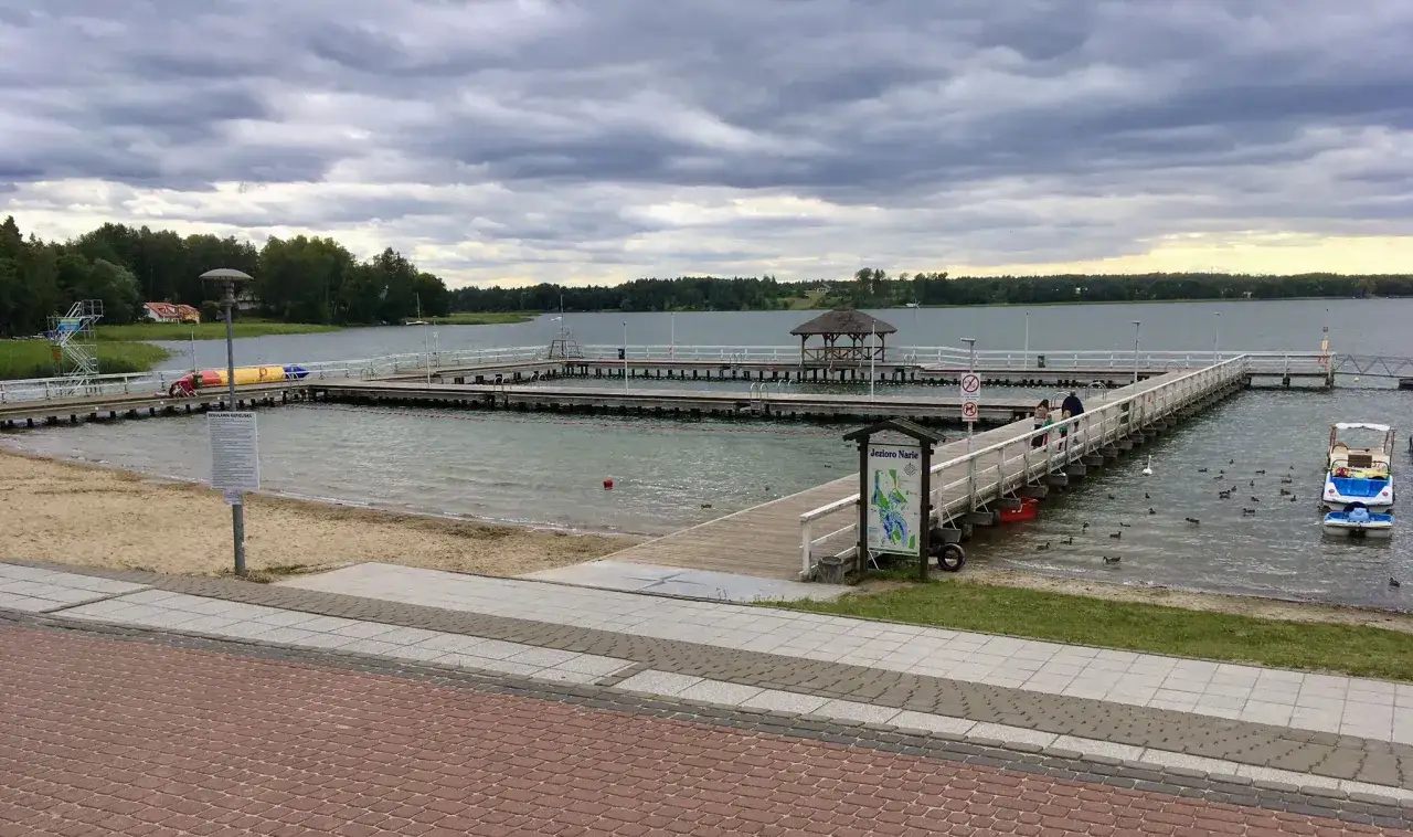 Miasto nad jeziorem Skiertąg z drewnianymi pomostami, plażą i kaczkami pływającymi w wodzie.