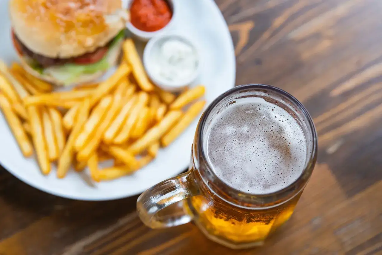 Un succulento hamburger con patatine fritte e una birra ghiacciata, un classico abbinamento per una serata perfetta.